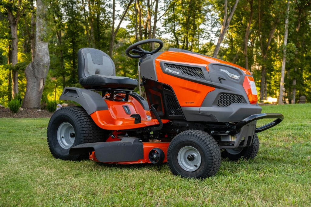 An orange and gray riding lawn mower parked on a green lawn in front of trees